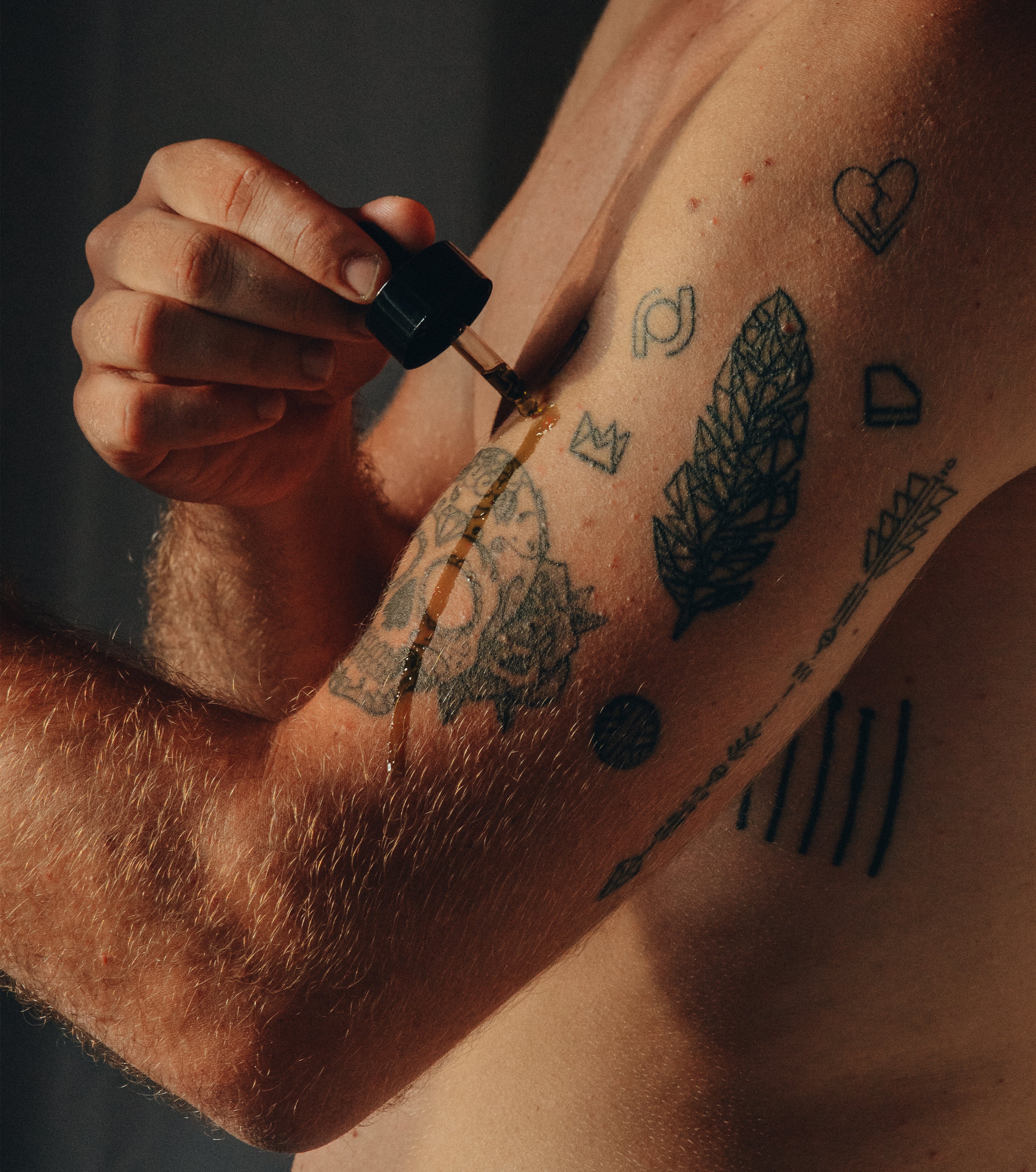Person applying CBD oil from a dropper on tattooed arm, showcasing skin care with hemp extract.