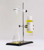 Botella de aceite corporal con CBD y jojoba en un soporte de laboratorio, con un embudo y frasco de vidrio.
