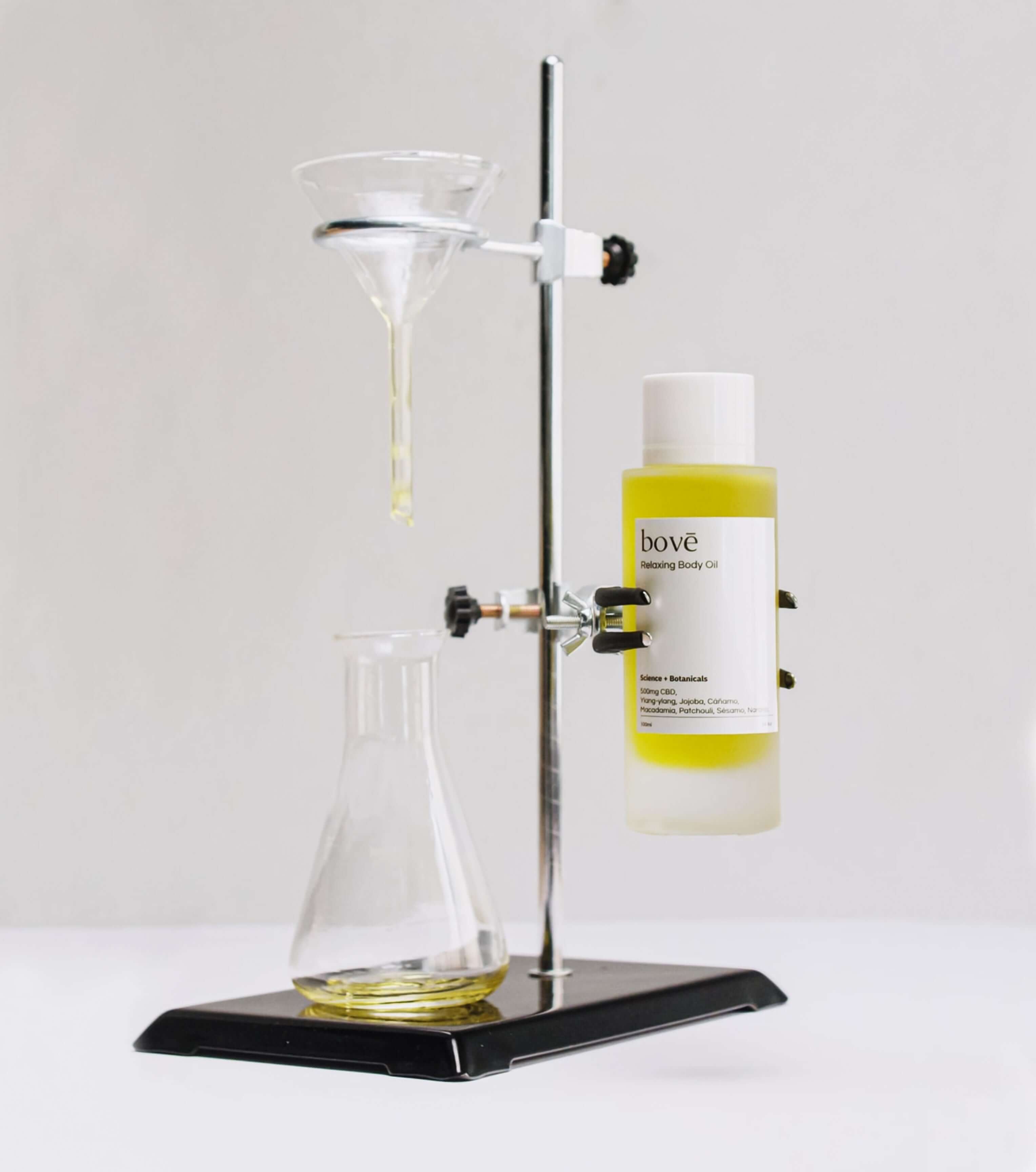 Botella de aceite corporal con CBD y jojoba en un soporte de laboratorio, con un embudo y frasco de vidrio.