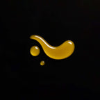 Gotas de aceite corporal con CBD y jojoba sobre fondo negro, mostrando su textura y color natural.