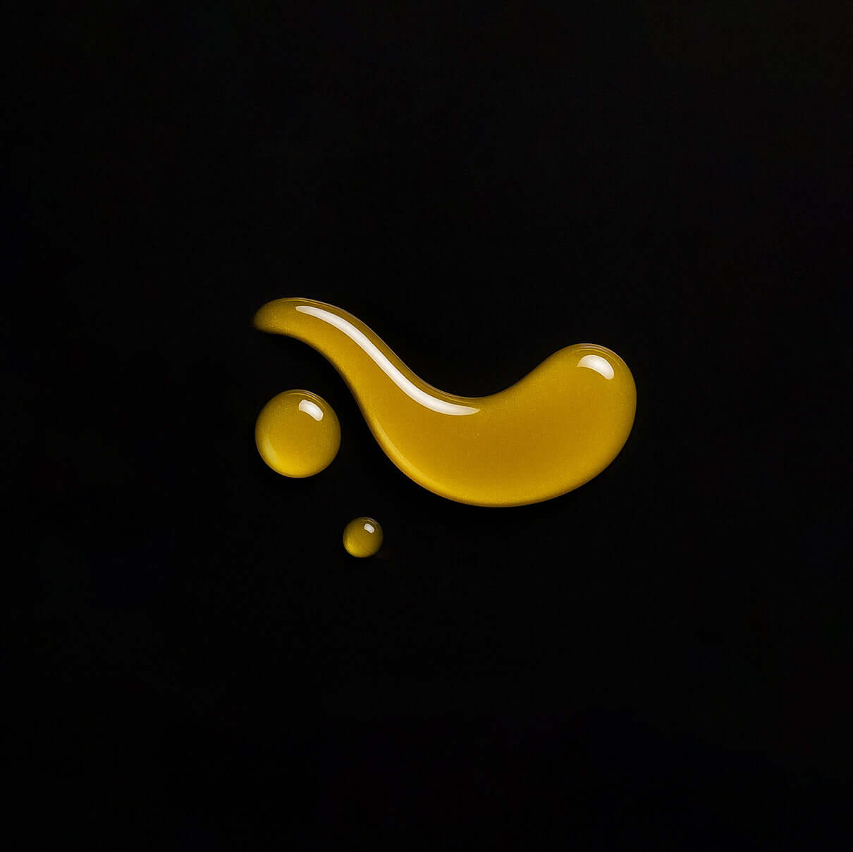 Gotas de aceite corporal con CBD y jojoba sobre fondo negro, mostrando su textura y color natural.
